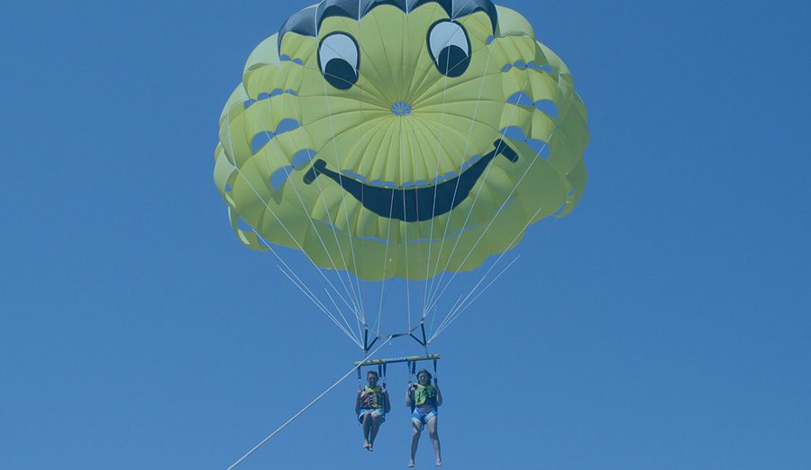 Two people parasailing under a smiley-face parachute